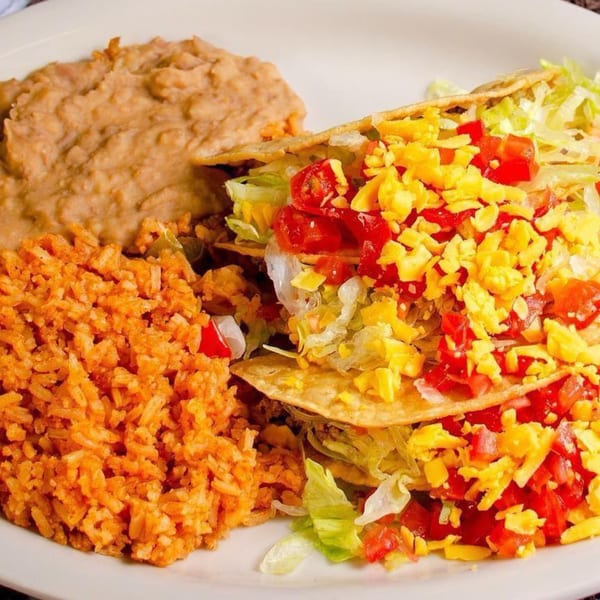 Two crispy tacos with lettuce, tomatoes, and cheese, served with refried beans and Mexican rice.
