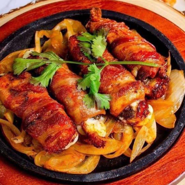 Bacon-wrapped shrimp and melted cheese on a sizzling skillet with sautéed onions, garnished with cilantro.