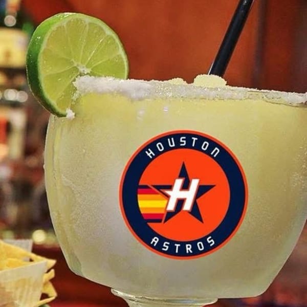 A Houston Astros branded margarita with a lime wedge and salt rim, with tortilla chips in the background.