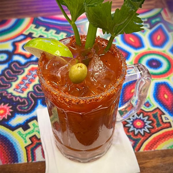 A Michelada cocktail in a mug with a chili-lime rim, garnished with celery, lime, and an olive.