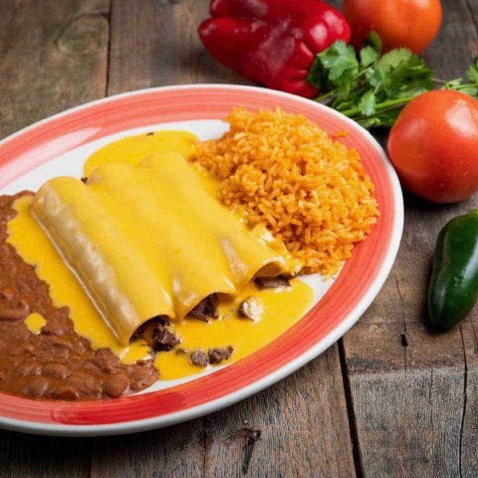 Three cheesy enchiladas with rice and refried beans on a white and red plate, with vegetables.