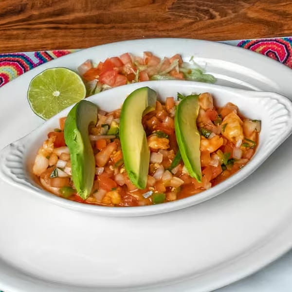 Shrimp ceviche with avocado slices, lime, and a side of lettuce and tomato on a white plate.