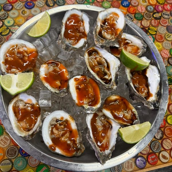 A dozen fresh oysters on the half shell with red sauce and lime wedges, served on ice.