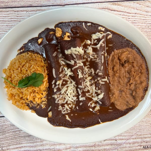 Three enchiladas covered in dark mole sauce and shredded cheese, with rice and refried beans.