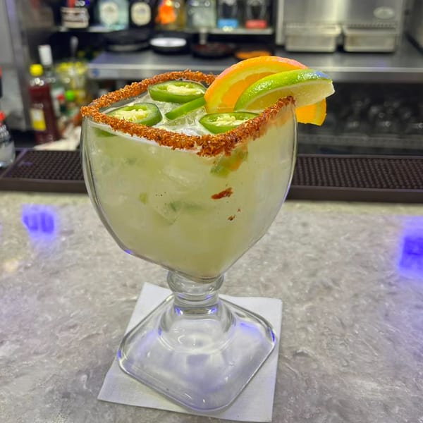 Spicy margarita with chili-lime rim, jalapeño slices, and citrus garnishes on a bar.