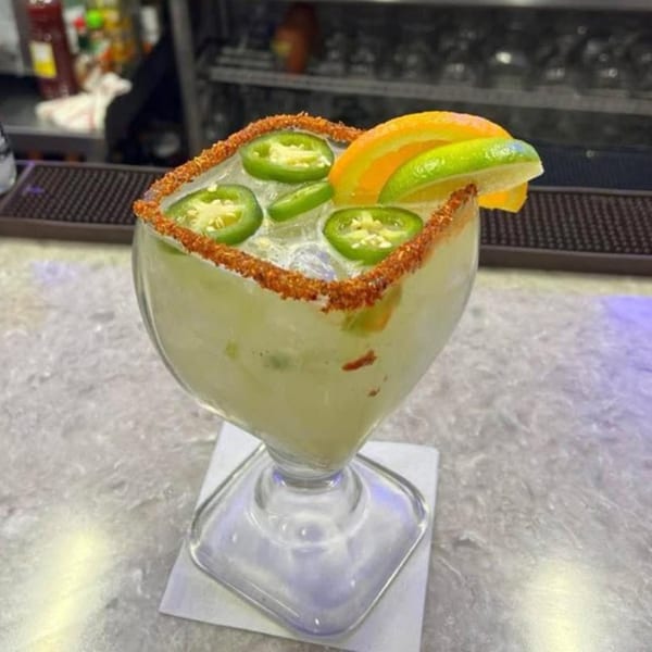 Spicy margarita with jalapeño slices, orange, and lime garnishes, rimmed with chili salt.