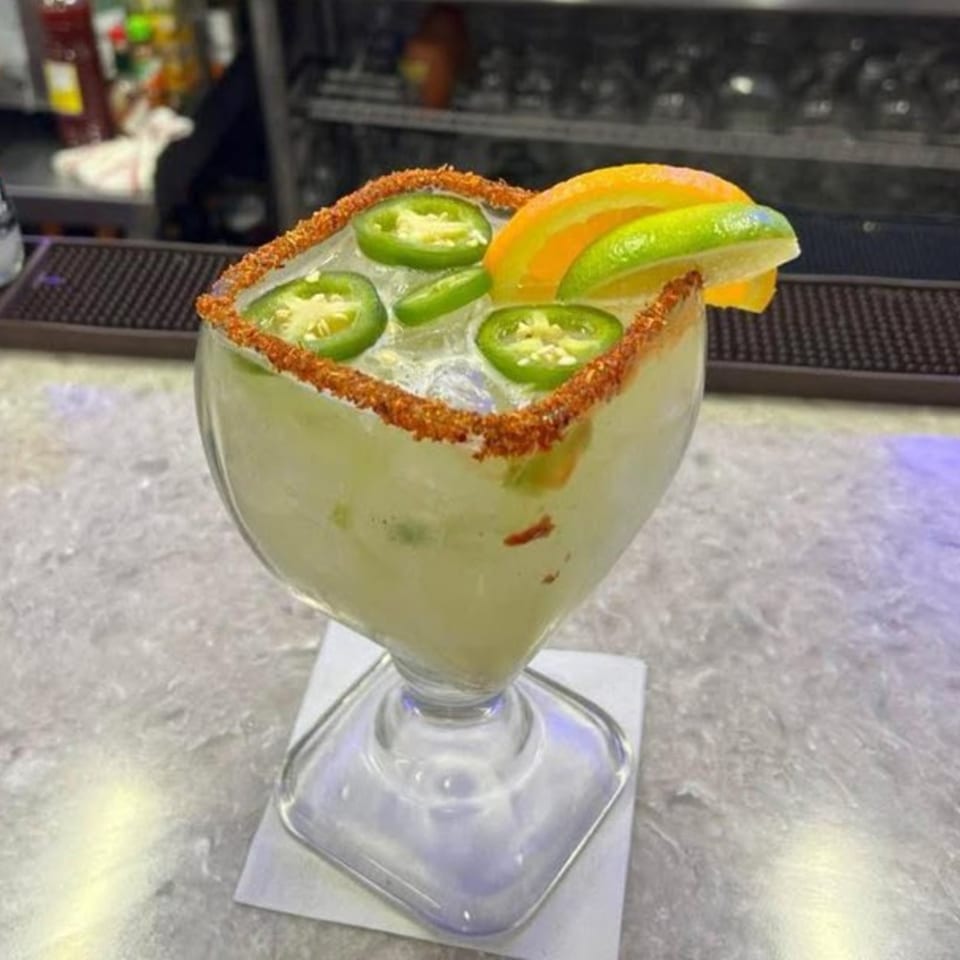 Spicy margarita with jalapeño slices, orange, and lime garnishes, rimmed with chili salt.