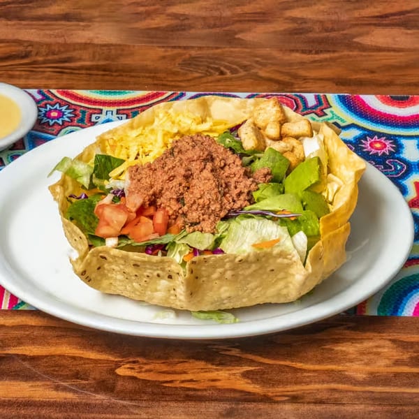 Taco salad with ground beef, lettuce, tomatoes, cheese, and avocado in a crispy tortilla bowl.