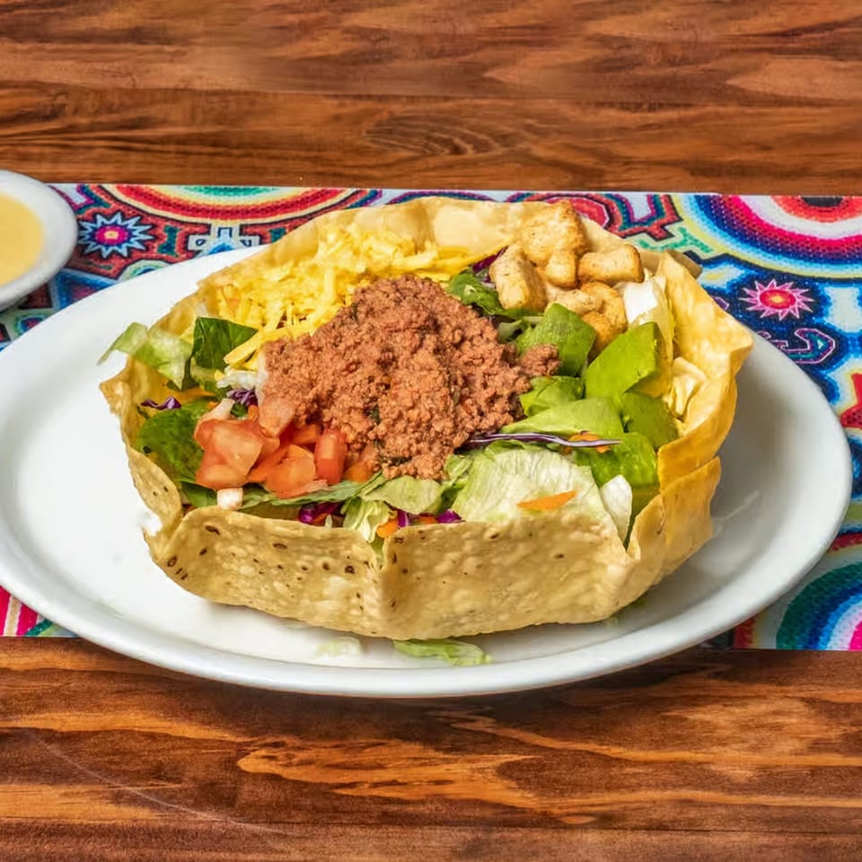 Taco salad with ground beef, lettuce, tomatoes, cheese, and avocado in a crispy tortilla bowl.